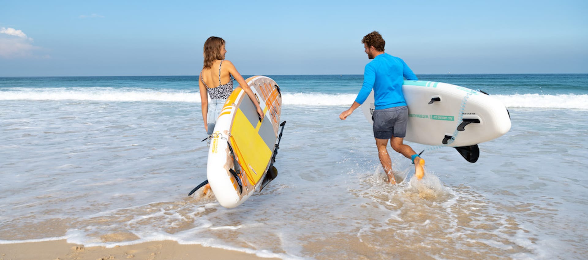 Two people walking into the water while carrying stand up paddleboards