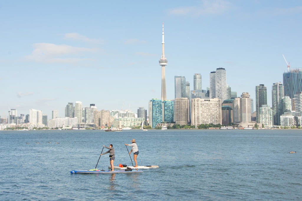 Two women paddleboard on Lake Ontario with the Toronto skyline in the background