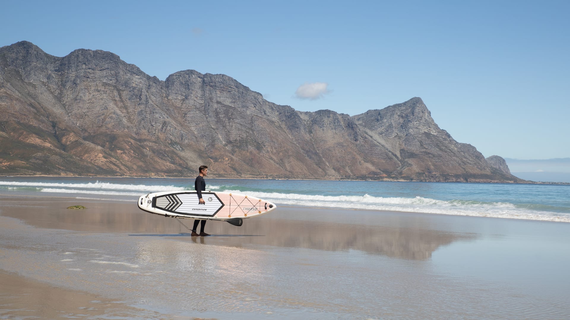 Man carrying a Thurso Surf paddleboard to the shoreline