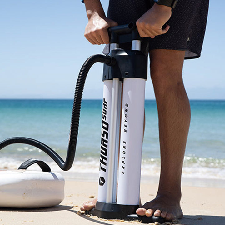 Person using a Thrurso paddleboard pump on a beach with ocean in the background